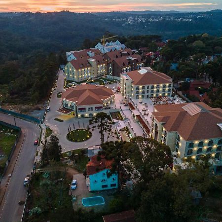 Buona Vitta Gramado Resort & Spa By Gramado Parks 외부 사진 The photo shows an aerial view of a hotel complex set in a hilly, wooded area. The buildings feature a mix of architectural styles with several structures, including a central round pavilion. Surrounding the buildings are well-maintained gardens and 