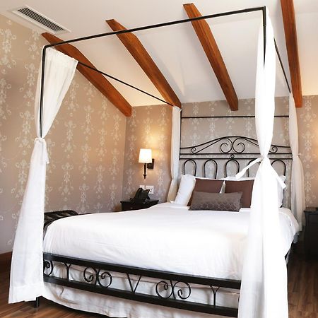 Buona Vitta Gramado Resort & Spa By Gramado Parks 외부 사진 The photo shows a beautifully designed bedroom featuring a four-poster bed with a metal frame and flowing white curtains. The bed is adorned with white bedding and brown decorative pillows. The room has wooden beams on the ceiling and is decorated wi