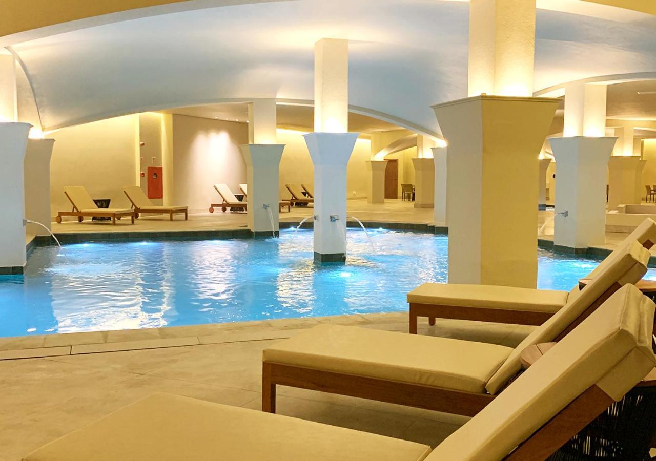 Buona Vitta Gramado Resort & Spa By Gramado Parks 외부 사진 The photo shows an indoor spa or relaxation area with a tranquil atmosphere. There is a large swimming pool with clear blue water, illuminated by soft lighting. Surrounding the pool are several comfortable lounge chairs. The architecture features ele