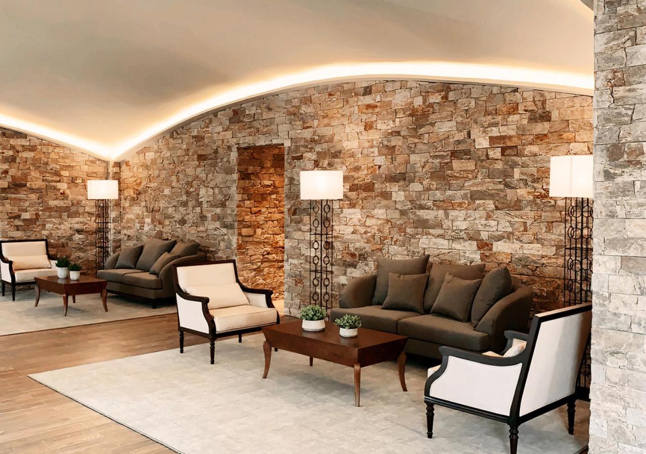 Buona Vitta Gramado Resort & Spa By Gramado Parks 외부 사진 The photo shows a stylish and modern lounge area. The walls are made of natural stone, creating a warm and inviting atmosphere. There are two comfortable sofas in a muted gray color arranged around a wooden coffee table. Flanking the sofas are elegan