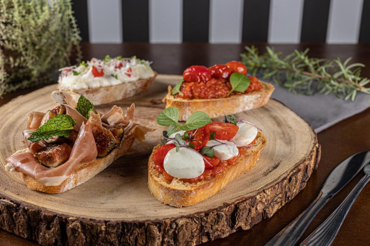 Buona Vitta Gramado Resort & Spa By Gramado Parks 외부 사진 The photo displays a wooden serving platter featuring four different types of bruschetta. Each piece of bruschetta is topped with various ingredients:

1. The top left has a creamy spread, possibly cheese or ricotta, garnished with fresh herbs and sm