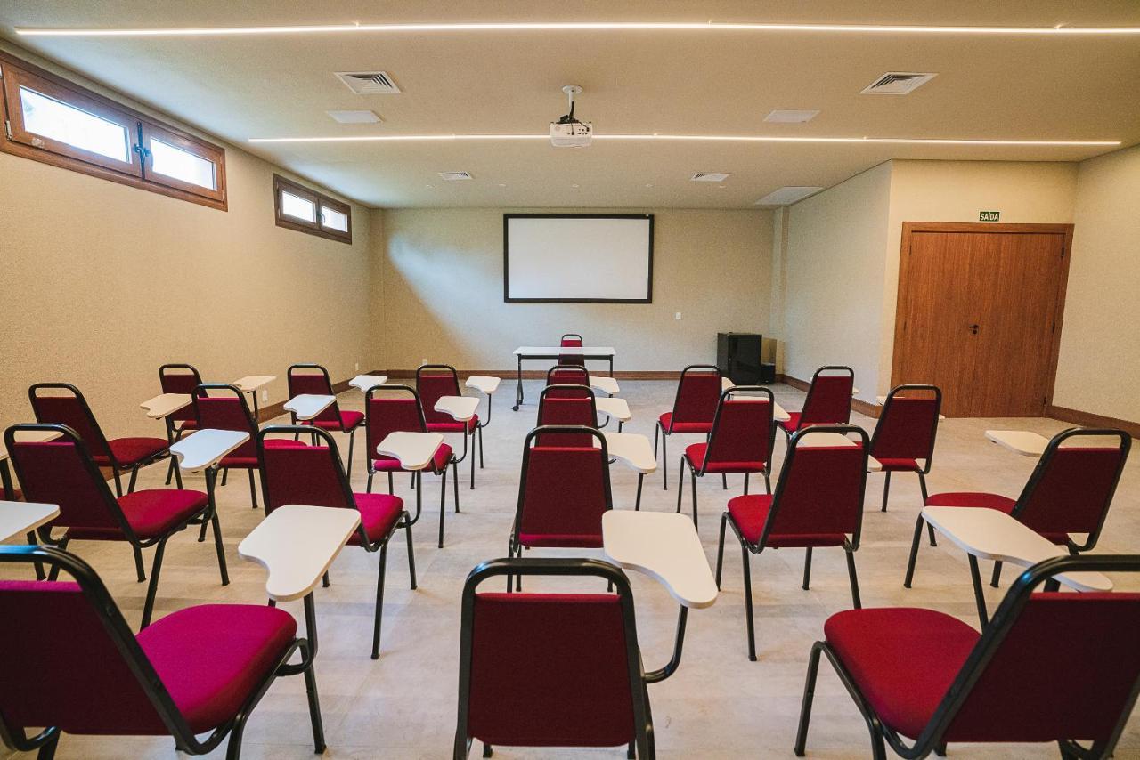 Buona Vitta Gramado Resort & Spa By Gramado Parks 외부 사진 The photo shows a classroom or meeting room set up for a presentation or lecture. It features several rows of red chairs, each with a small writing surface attached. There is a blank screen mounted on the wall at the front of the room, likely for dis