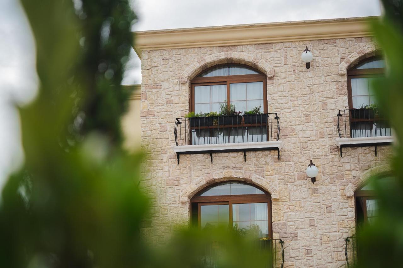 Buona Vitta Gramado Resort & Spa By Gramado Parks 외부 사진 The photo depicts a stone building with a textured exterior. It features several windows with wooden frames. Each window has a small balcony adorned with decorative plants. There are also wall-mounted light fixtures flanking the windows. In the foreg