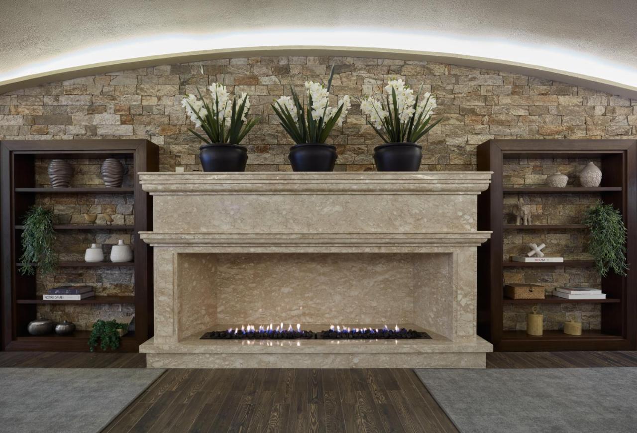 Buona Vitta Gramado Resort & Spa By Gramado Parks 외부 사진 The photo shows a modern fireplace design built into a wall with a textured stone background. The fireplace is made of a light-colored stone and features a long, narrow gas flame visible at the bottom. Above the fireplace, there are two large potted 