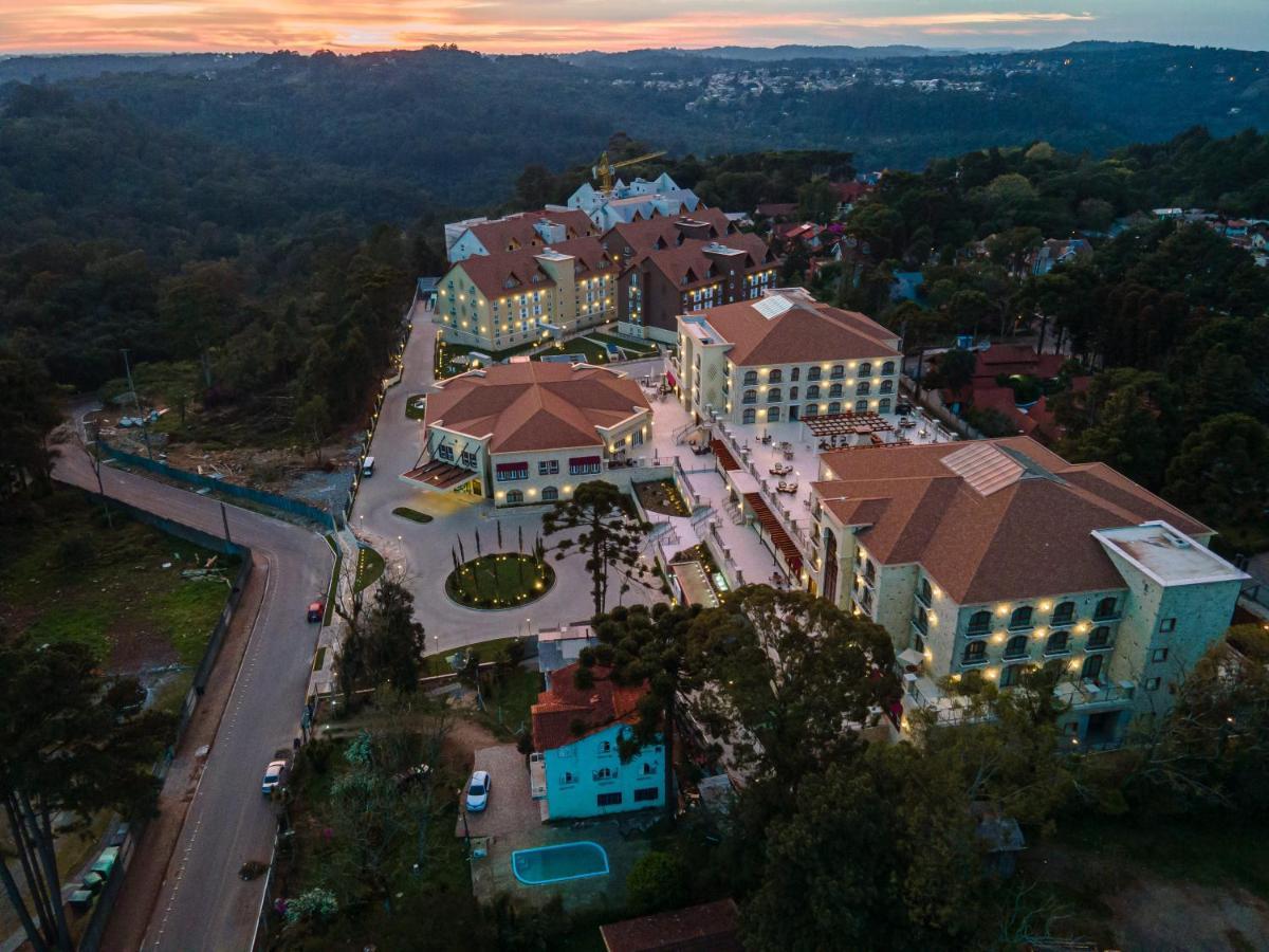Buona Vitta Gramado Resort & Spa By Gramado Parks 외부 사진 The photo shows an aerial view of a hotel complex set in a hilly, wooded area. The buildings feature a mix of architectural styles with several structures, including a central round pavilion. Surrounding the buildings are well-maintained gardens and 