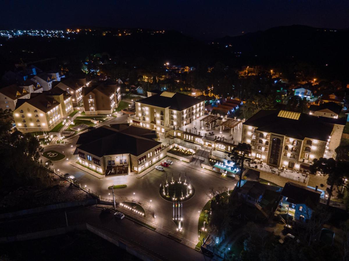 Buona Vitta Gramado Resort & Spa By Gramado Parks 외부 사진 The photo shows a beautifully lit resort or hotel complex taken at night. The buildings are well-illuminated, highlighting their architecture. There is a circular area with a fountain at the center, surrounded by pathways that connect various parts o
