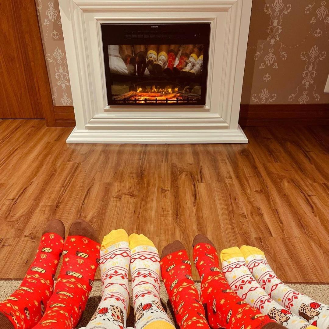 Buona Vitta Gramado Resort & Spa By Gramado Parks 외부 사진 The photo shows a cozy indoor setting with a warm fireplace. In the foreground, several pairs of feet are displayed, each wearing brightly colored socks with various patterns. The socks include red, yellow, and white designs, contributing to a cheerf