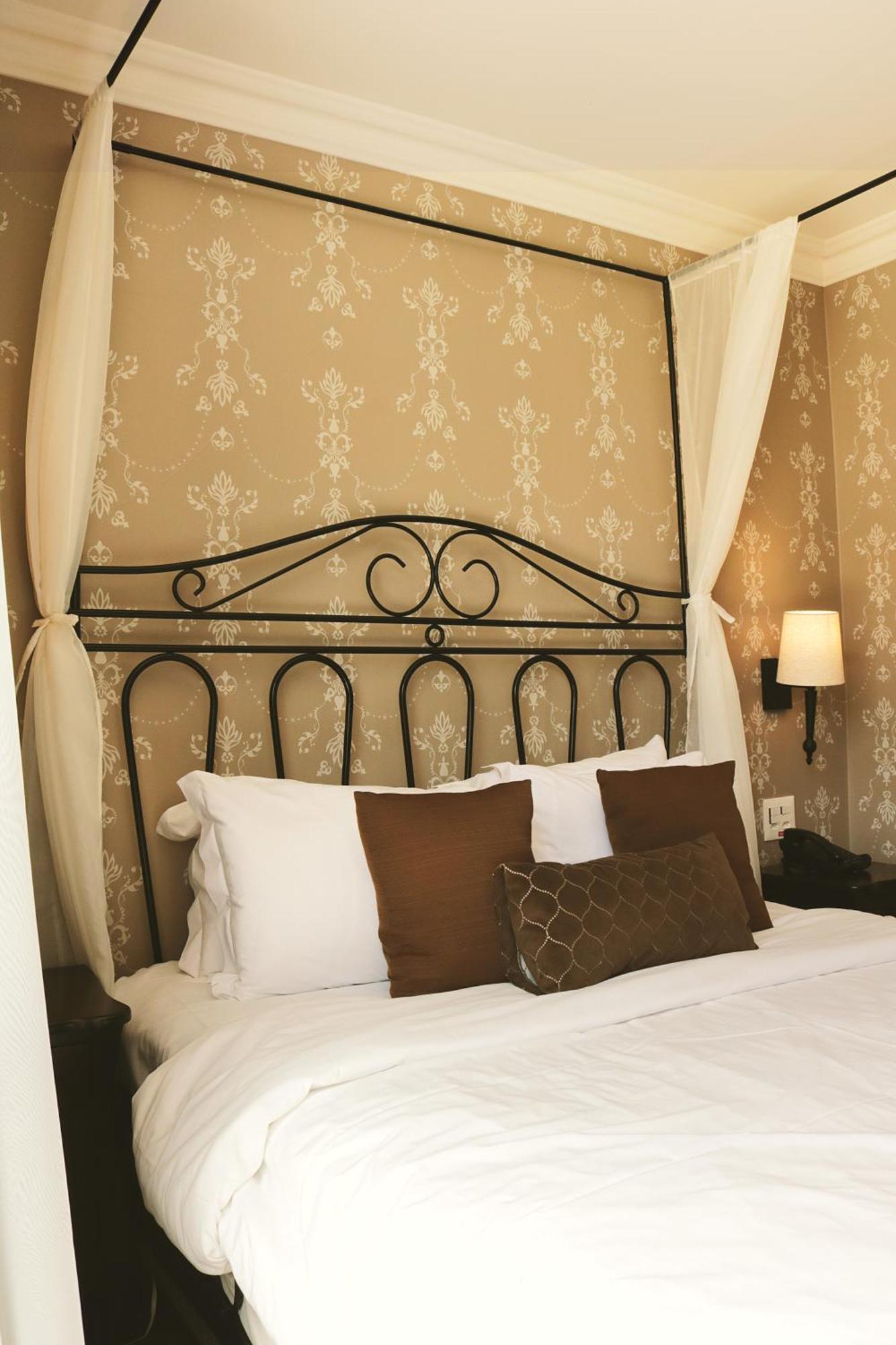 Buona Vitta Gramado Resort & Spa By Gramado Parks 외부 사진 The photo shows a cozy bedroom setup featuring a decorative metal bed frame with a scroll design as the headboard. The bed is adorned with several white pillows and two brown decorative cushions. The wall behind the bed is covered with a light-colore