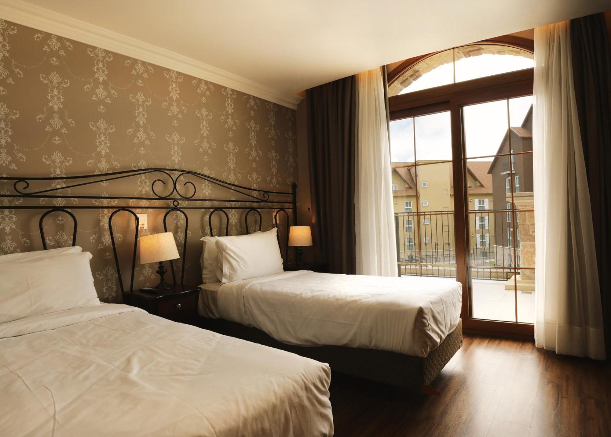 Buona Vitta Gramado Resort & Spa By Gramado Parks 외부 사진 The photo shows a well-decorated hotel room featuring two beds. One bed is larger, likely a double bed, while the other is a single bed. The walls are adorned with a floral pattern, and there are bedside lamps next to the larger bed. Large windows wi