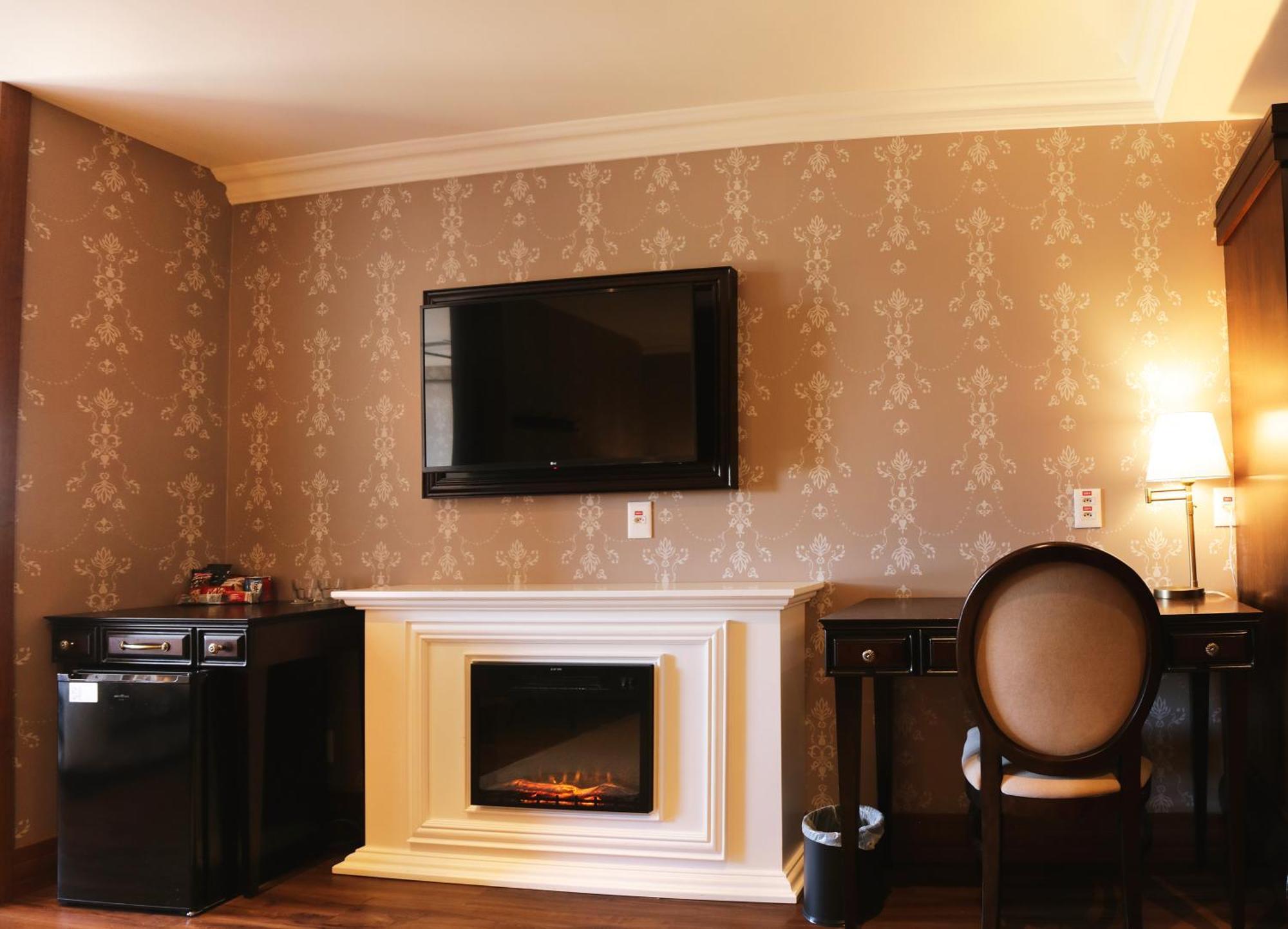 Buona Vitta Gramado Resort & Spa By Gramado Parks 외부 사진 The photo shows a cozy room featuring a decorative wall with a subtle pattern. On one side, there is a modern flat-screen television mounted on the wall. Below it, there is a stylish electric fireplace framed in white. Adjacent to the fireplace is a 