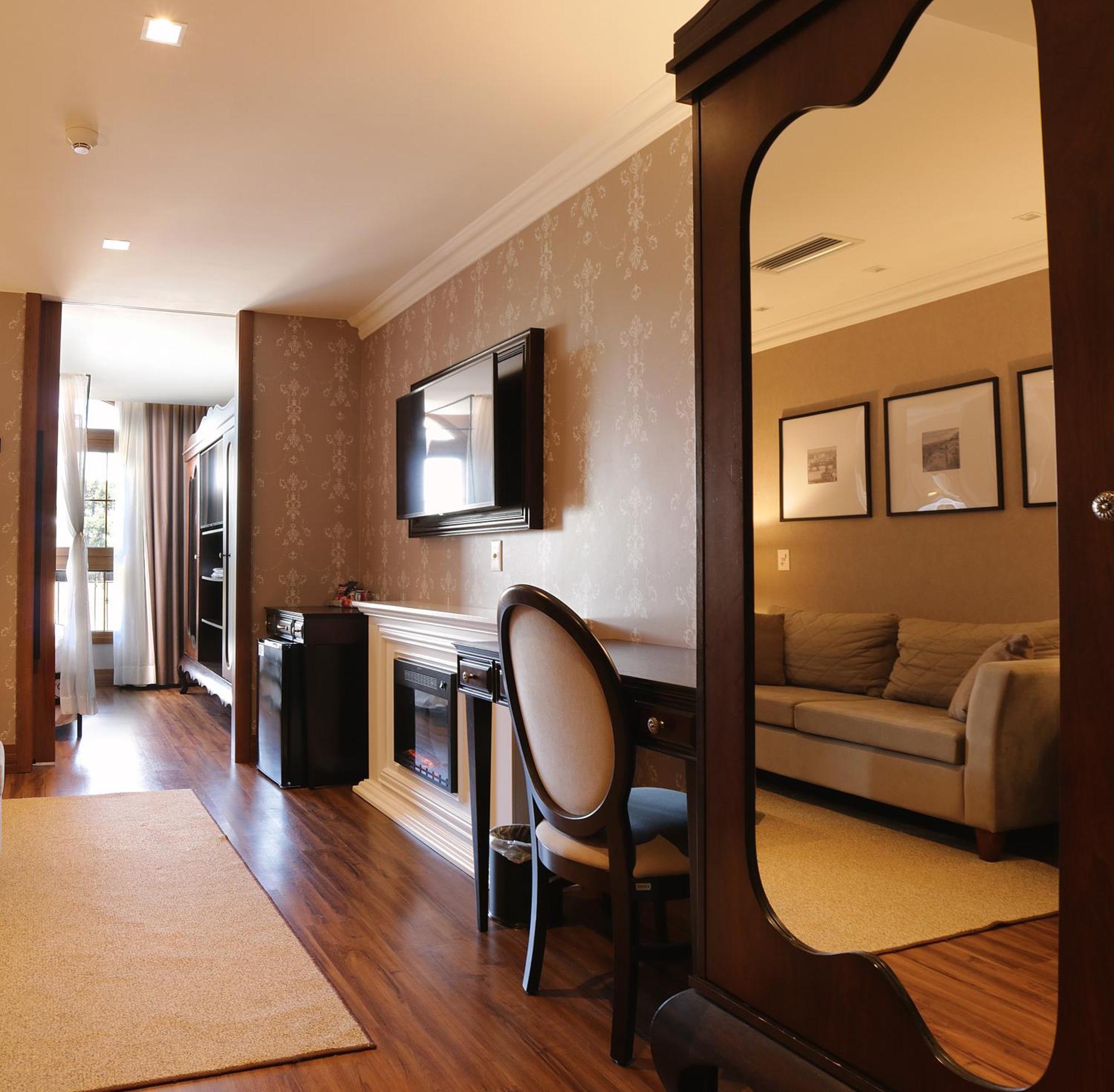 Buona Vitta Gramado Resort & Spa By Gramado Parks 외부 사진 The photo shows a well-decorated room that appears to be a living area or a hotel suite. In the foreground, there is a round chair and a desk. A large mirror reflects the living space, creating a sense of spaciousness. 

On the wall is a flat-screen 