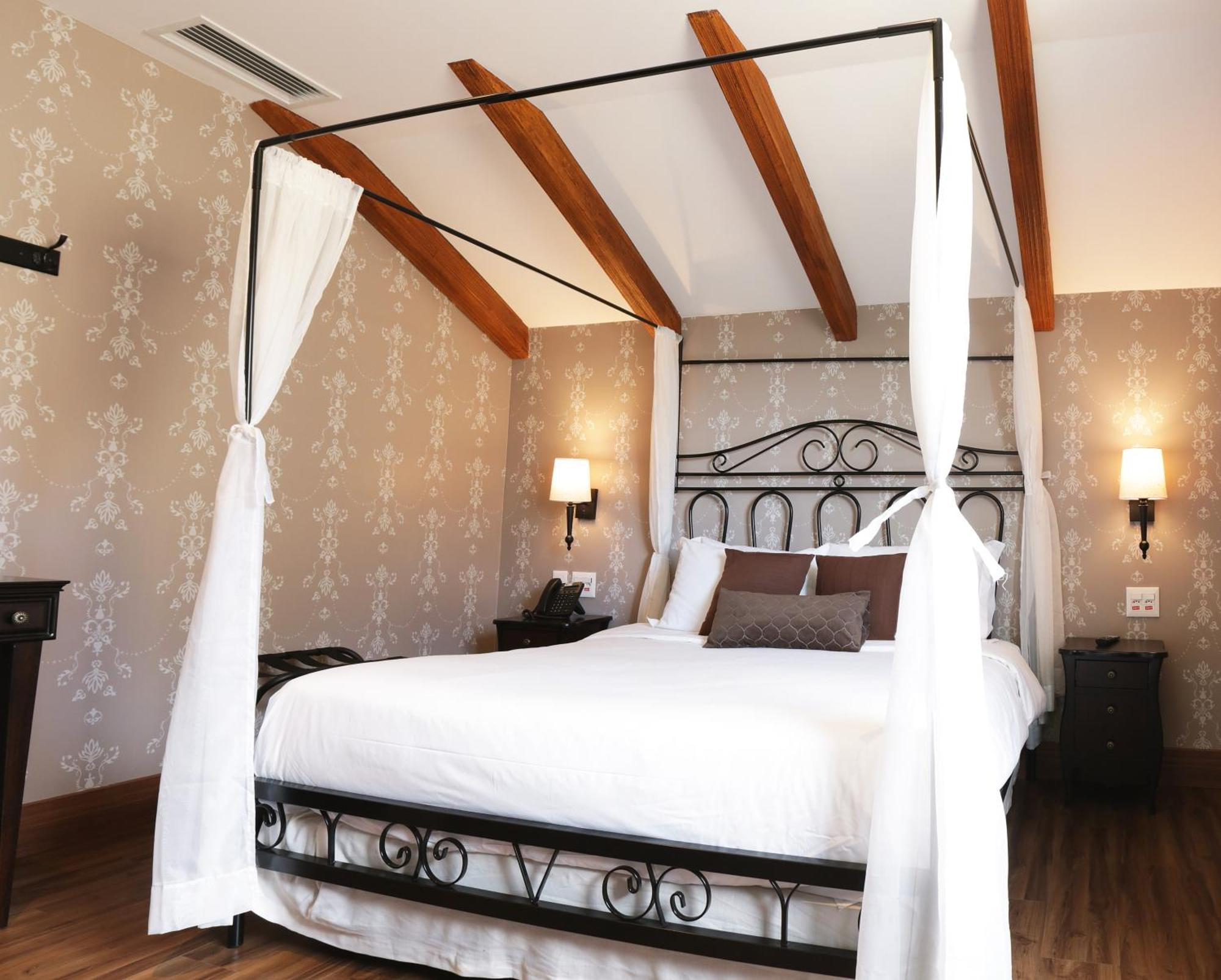 Buona Vitta Gramado Resort & Spa By Gramado Parks 외부 사진 The photo shows a beautifully designed bedroom featuring a four-poster bed with a metal frame and flowing white curtains. The bed is adorned with white bedding and brown decorative pillows. The room has wooden beams on the ceiling and is decorated wi