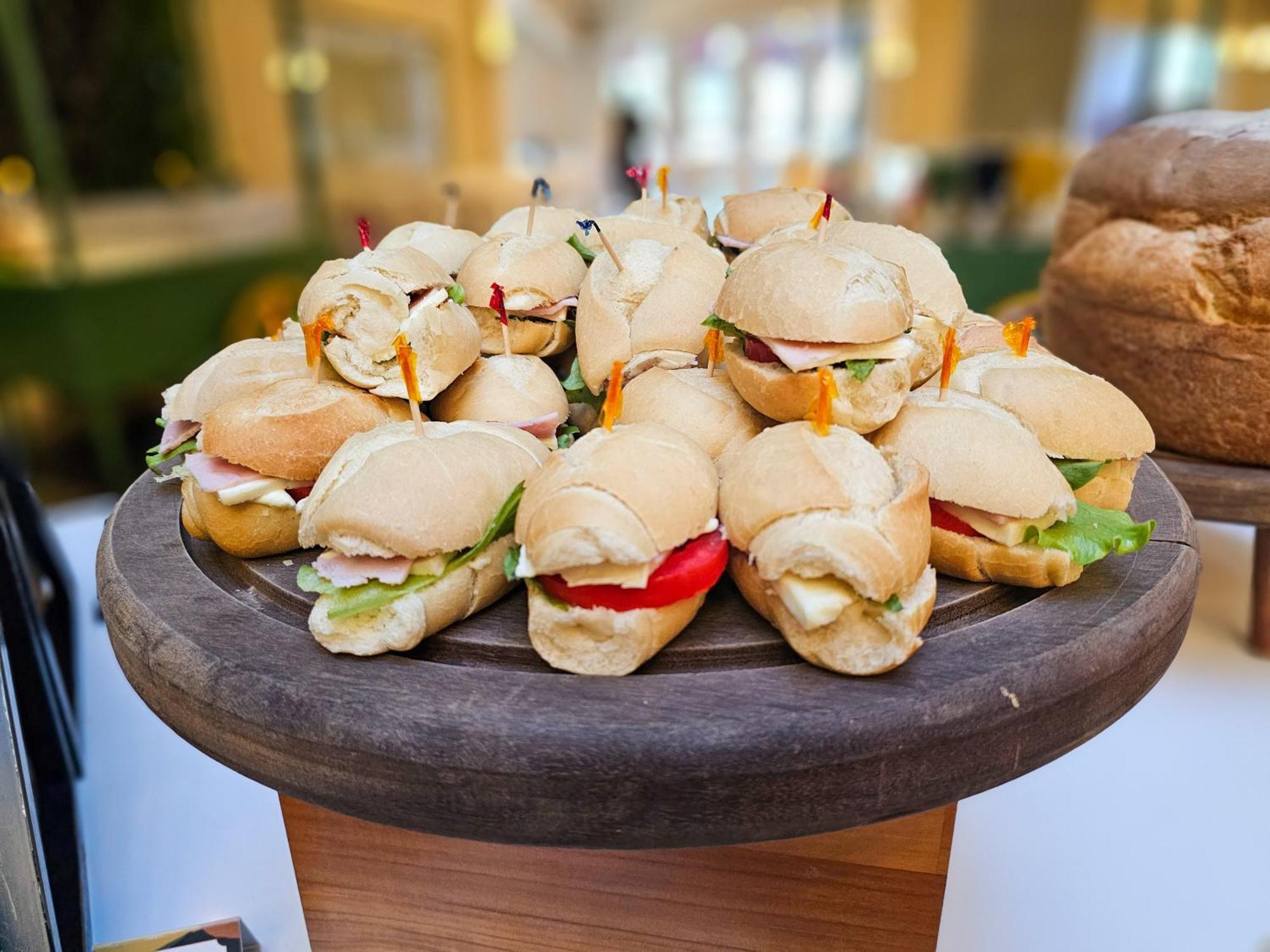 Buona Vitta Gramado Resort & Spa By Gramado Parks 외부 사진 The photo shows a platter of small sandwiches, likely sliders, arranged neatly on a wooden serving tray. These sandwiches have various fillings, including what appears to be ham, lettuce, and tomato. They are garnished with colorful toothpicks, and t